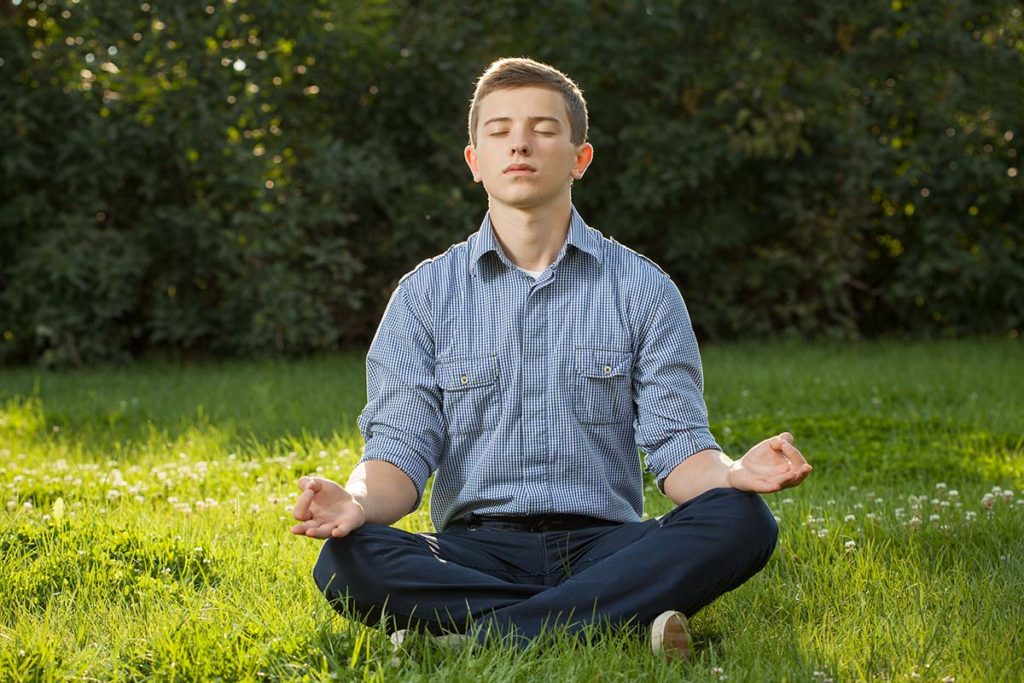 serene young man discovering the 5 benefits of meditation in a sunny green field