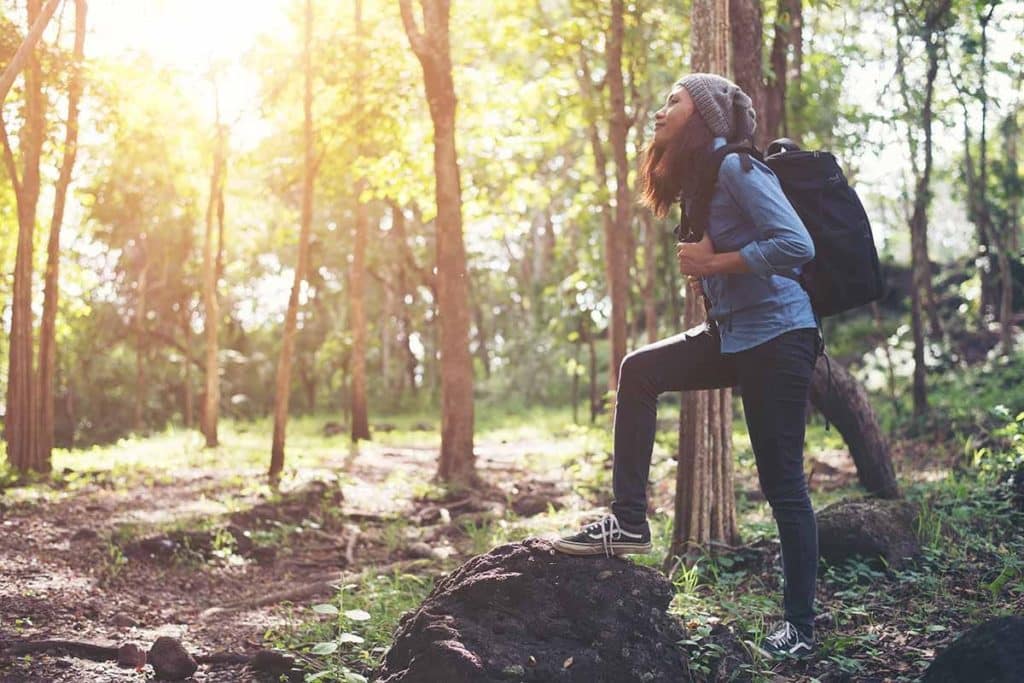 young woman hiking outside in the woods with sunlight streaming down as she discovers what are some good coping mechanisms