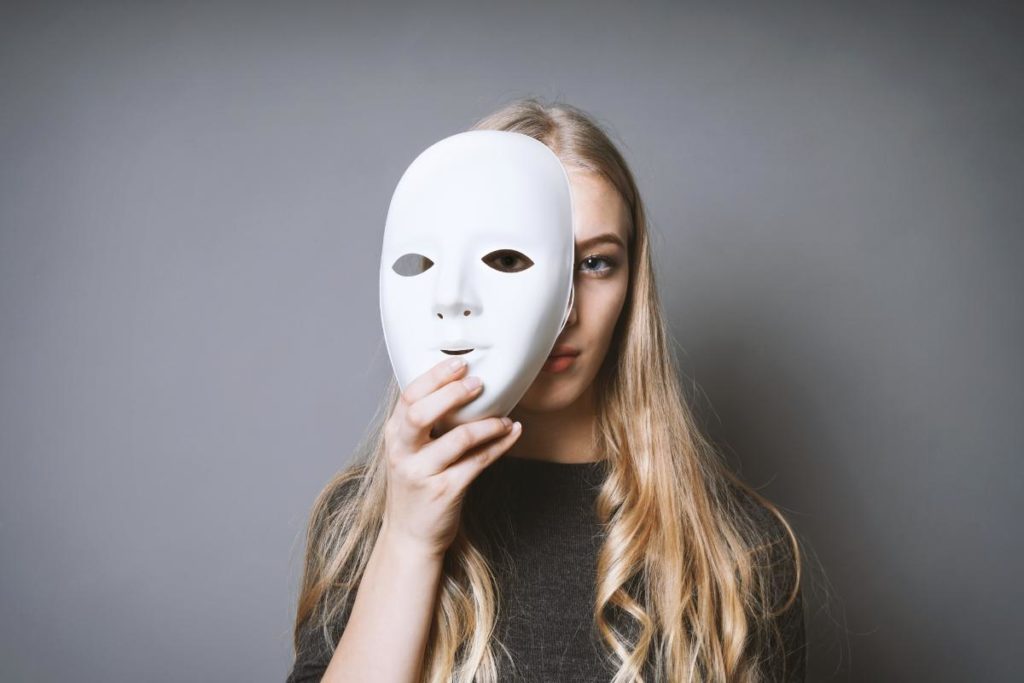 teenager holding stylized white theatre mask over her face as a symbol of the early signs of bipolar disorder
