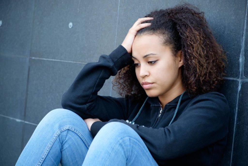teenager woman leaning against wall with head in her hands thinking about recognizing self harm in teens