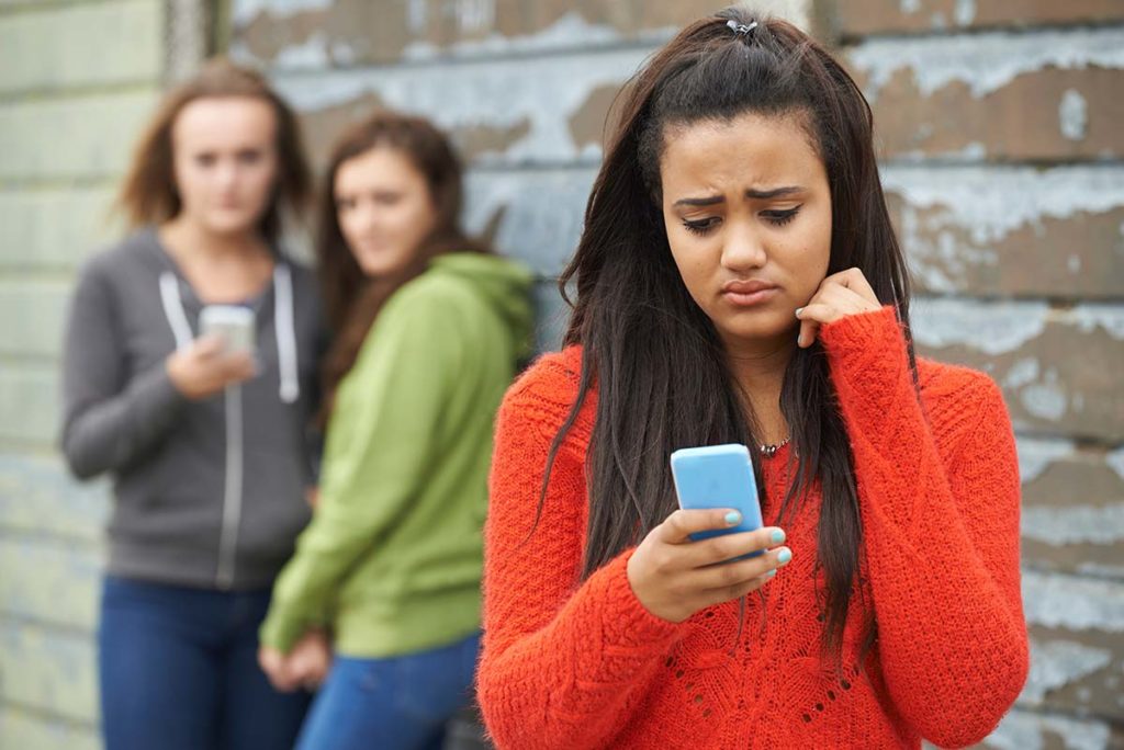 troubled teenage girl looking at phone while her parents worry is my child being bullied