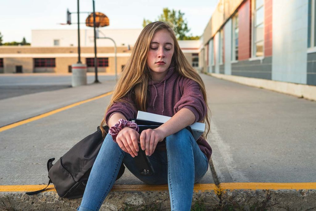 teenage girl sitting on street curb recognizing self harm in teens in herself