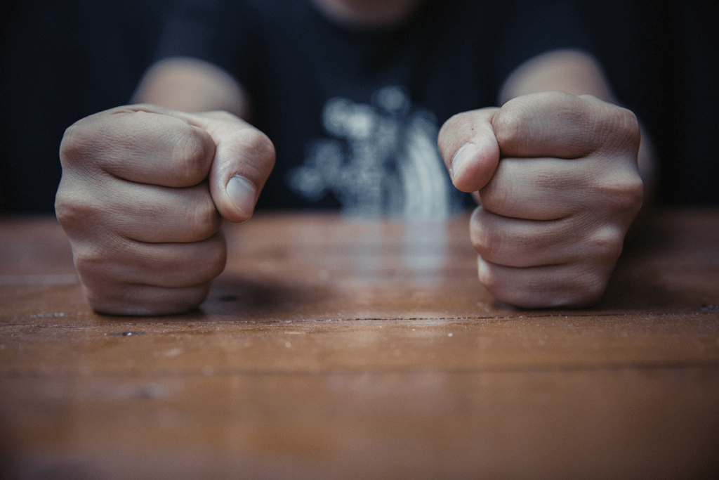 a teen who could benefit from an anger management program slams both fists on a table in a fit of rage