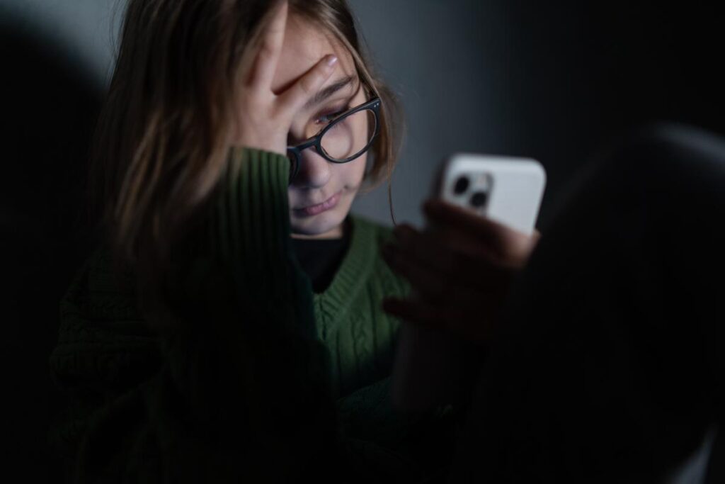 teenage girl sitting alone in dark room staring at her phone wondering can social media cause depression in teens