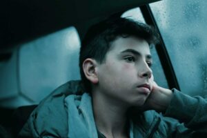 pensive teenage boy sitting in backseat of car on a dreary day attempting to employ the 7 mindfulness strategies for stress in teens