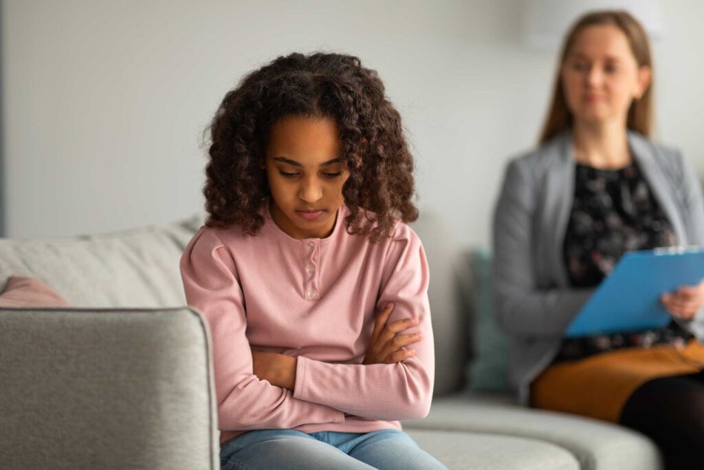 teenage girl looking dejected with her back towards therapist who is slowly understanding the long term effects of trauma in teens
