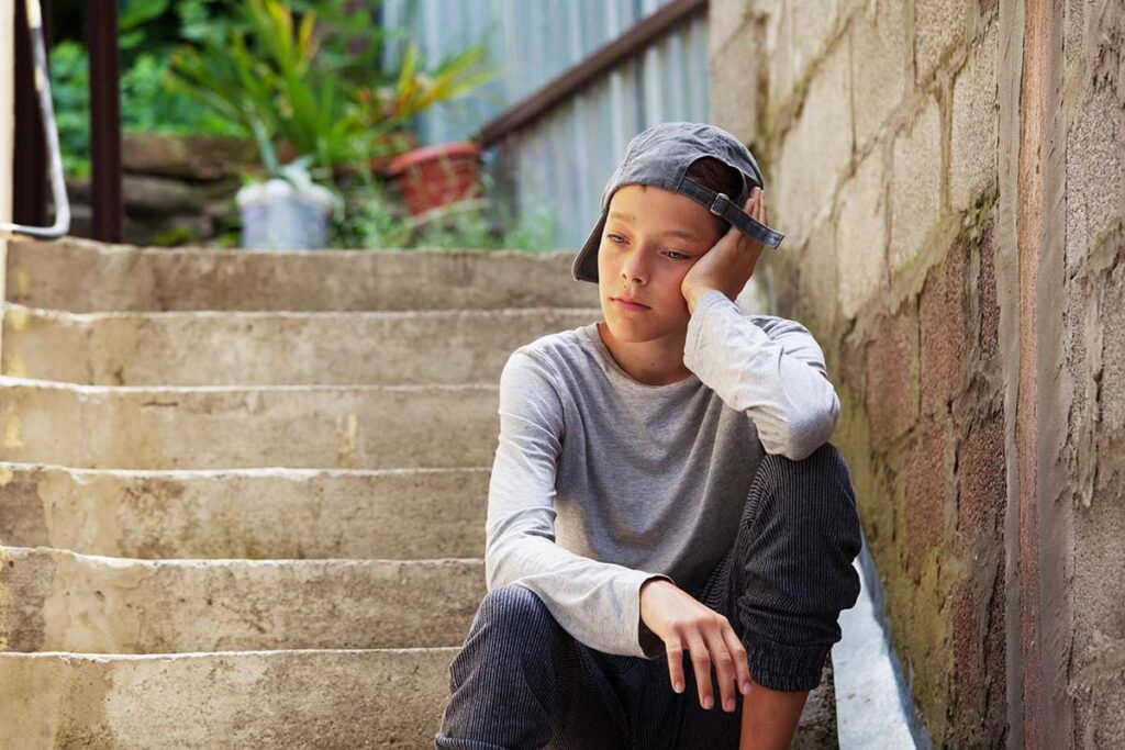 teenager sitting on steps outside in the sun contemplating the 3 reasons why a teen needs IOP treatment