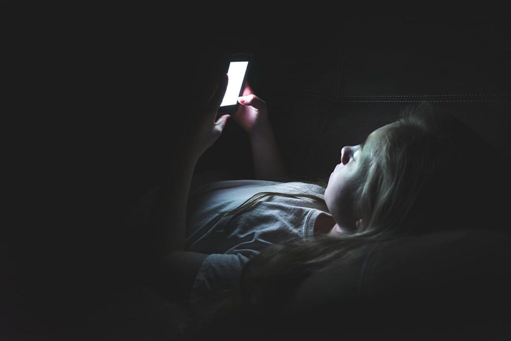 a teen lies in bed scrolling on their phone potentially leading to the effects of sleep deprivation