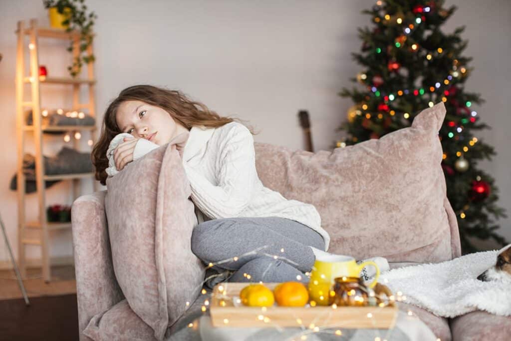 teenage girl slumped on couch with Christmas tree in background struggling to learn how to cope with holiday stress and anxiety