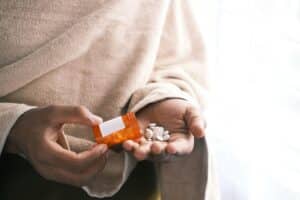 person dumping pills out of pill bottle into his hand